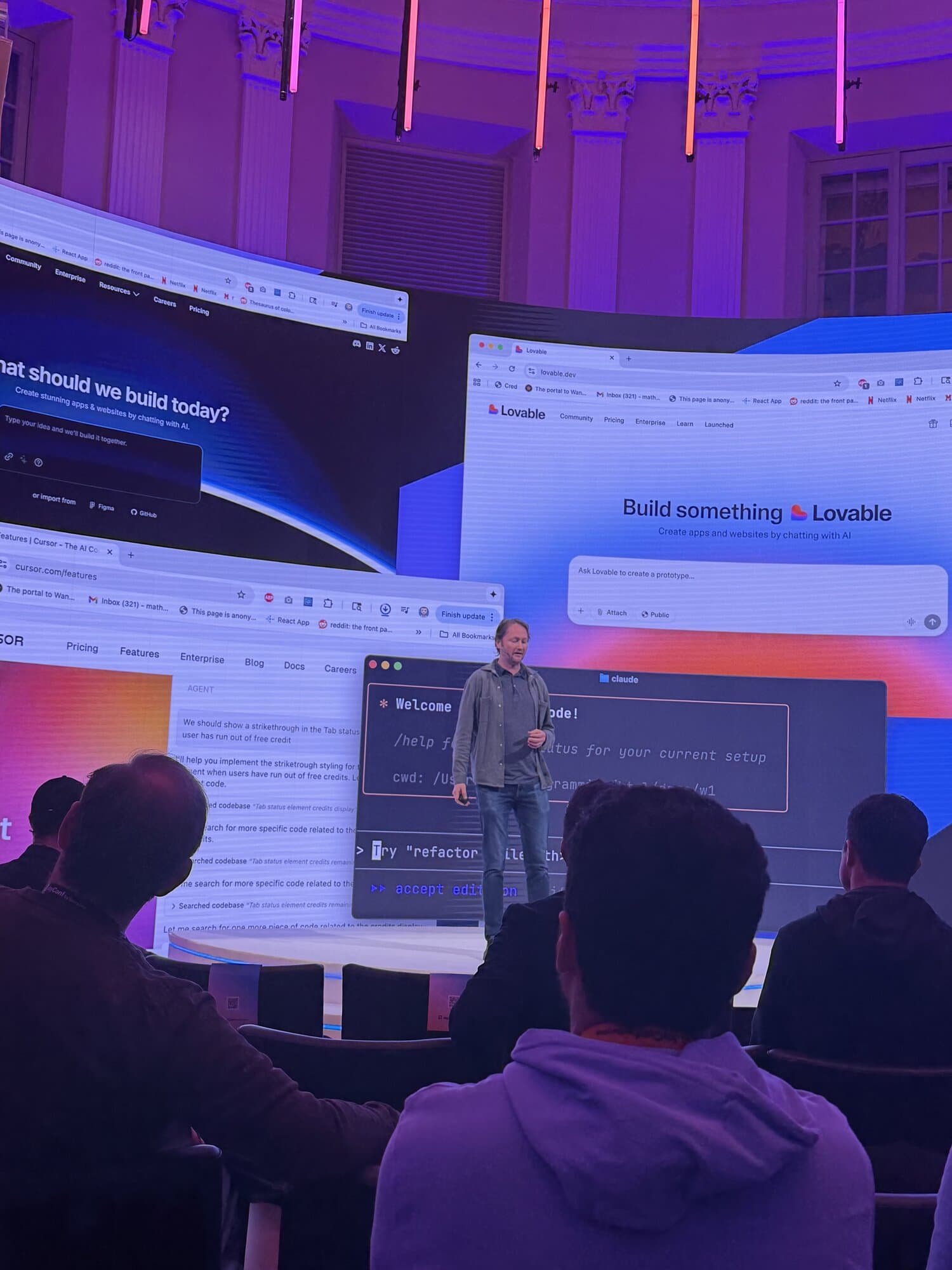 Mathias Billiman Netlify CEO stands on stage in front of a large screen displaying various AI and coding-related interfaces, while an audience watches attentively.