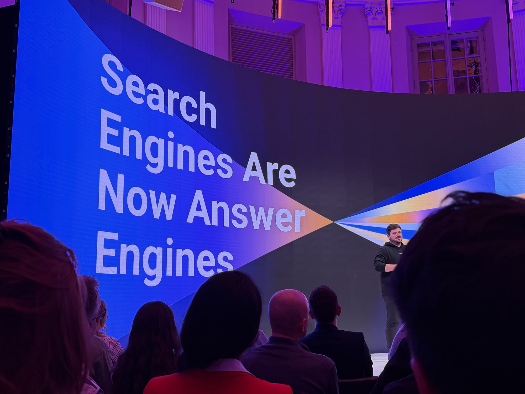 Dominik Angereron Storyblok CEO is stage is addressing an audience with a large screen behind them displaying the text "Search Engines Are Now Answer Engines."